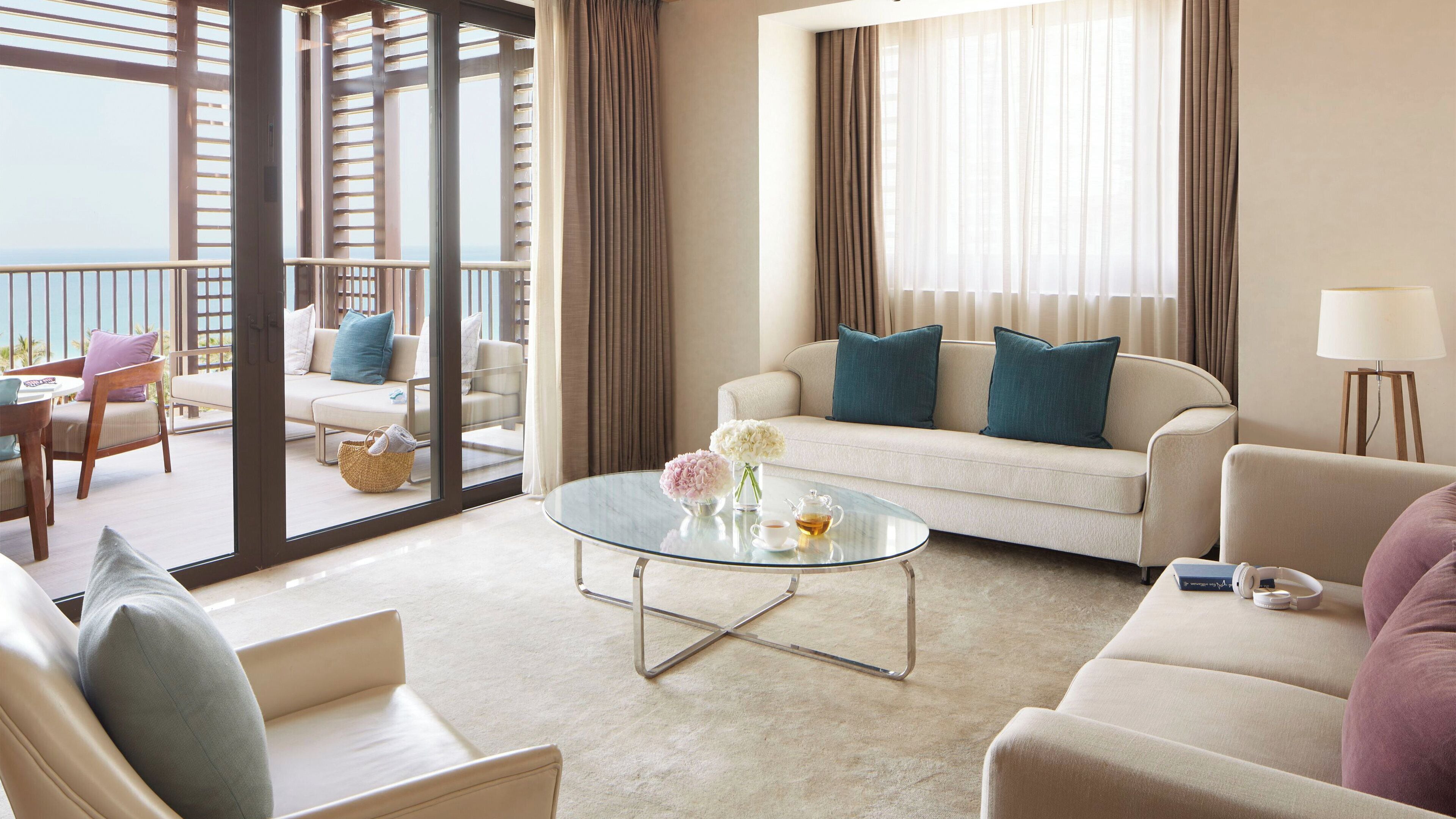 A modern hotel room with a balcony, a glass coffee table, and a sofa set.