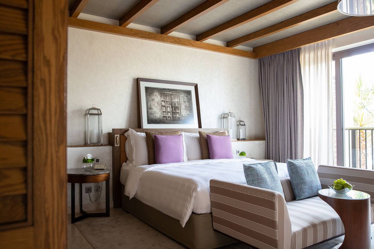 Habitación de hotel con una cama grande, un sofá, una mesita y una ventana con cortinas.