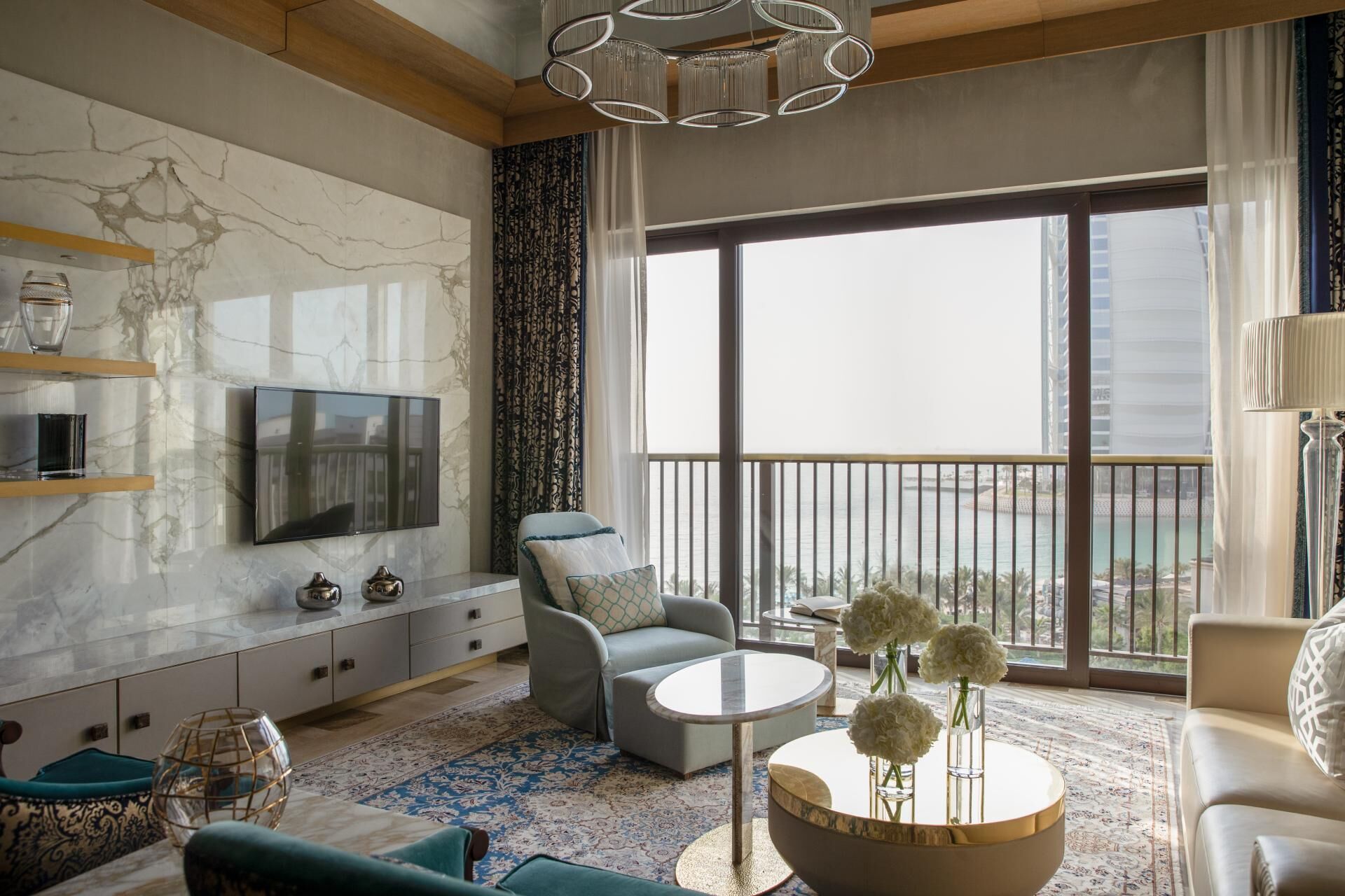 A modern living room with a TV, seating, a round coffee table, and a balcony with a view.