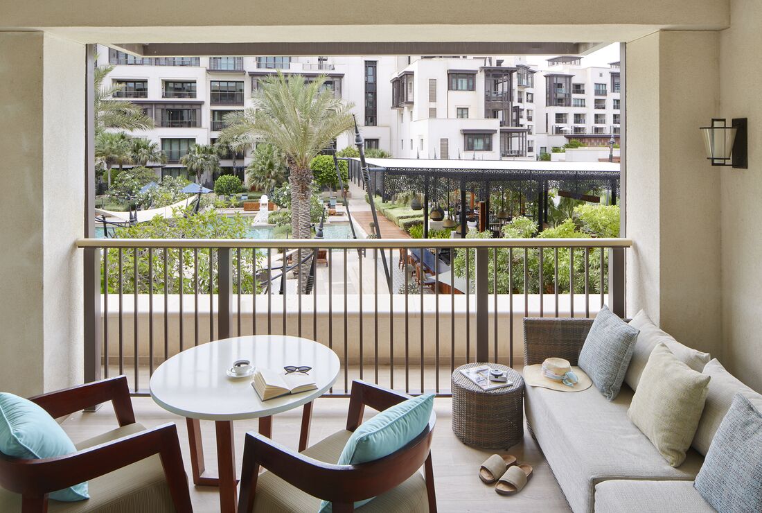 Un balcone con vista su un complesso di edifici moderni, un tavolo rotondo con sedie e un divano con cuscini.
