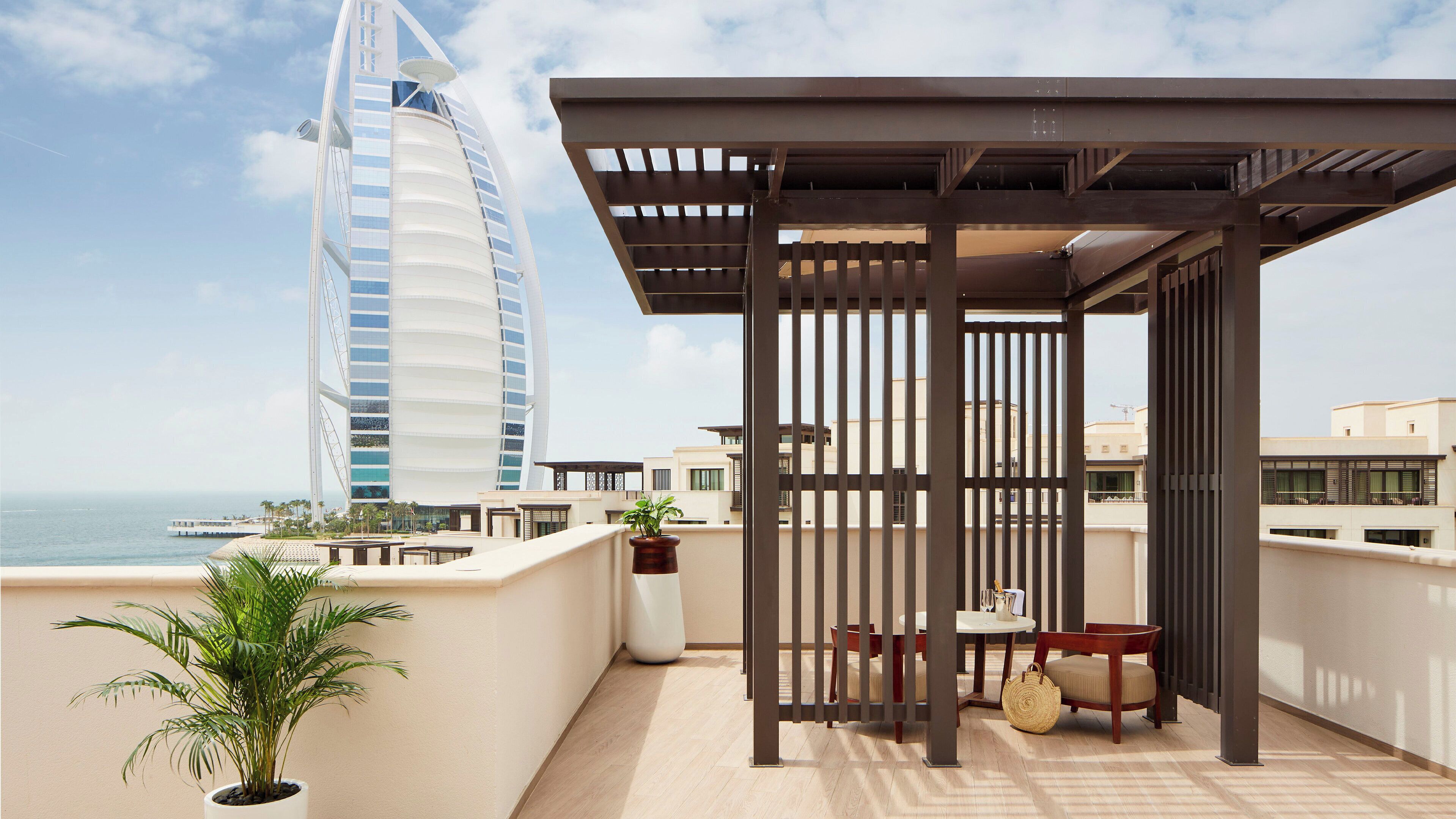 Una terrazza sul tetto con vista sull'hotel Burj Al Arab, una pergola, un tavolo con sedie e una pianta in vaso.