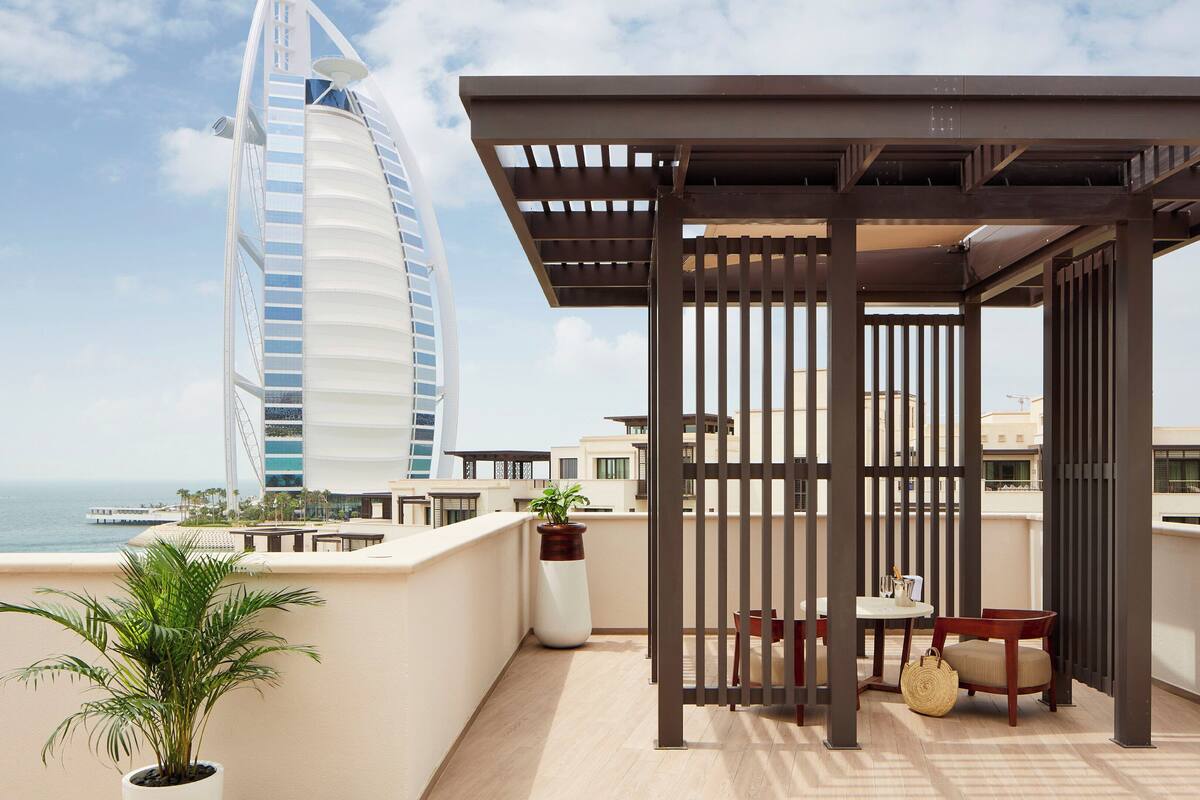 Una terraza en la azotea con vistas al hotel Burj Al Arab, una pérgola, una mesa con sillas y una planta en maceta.