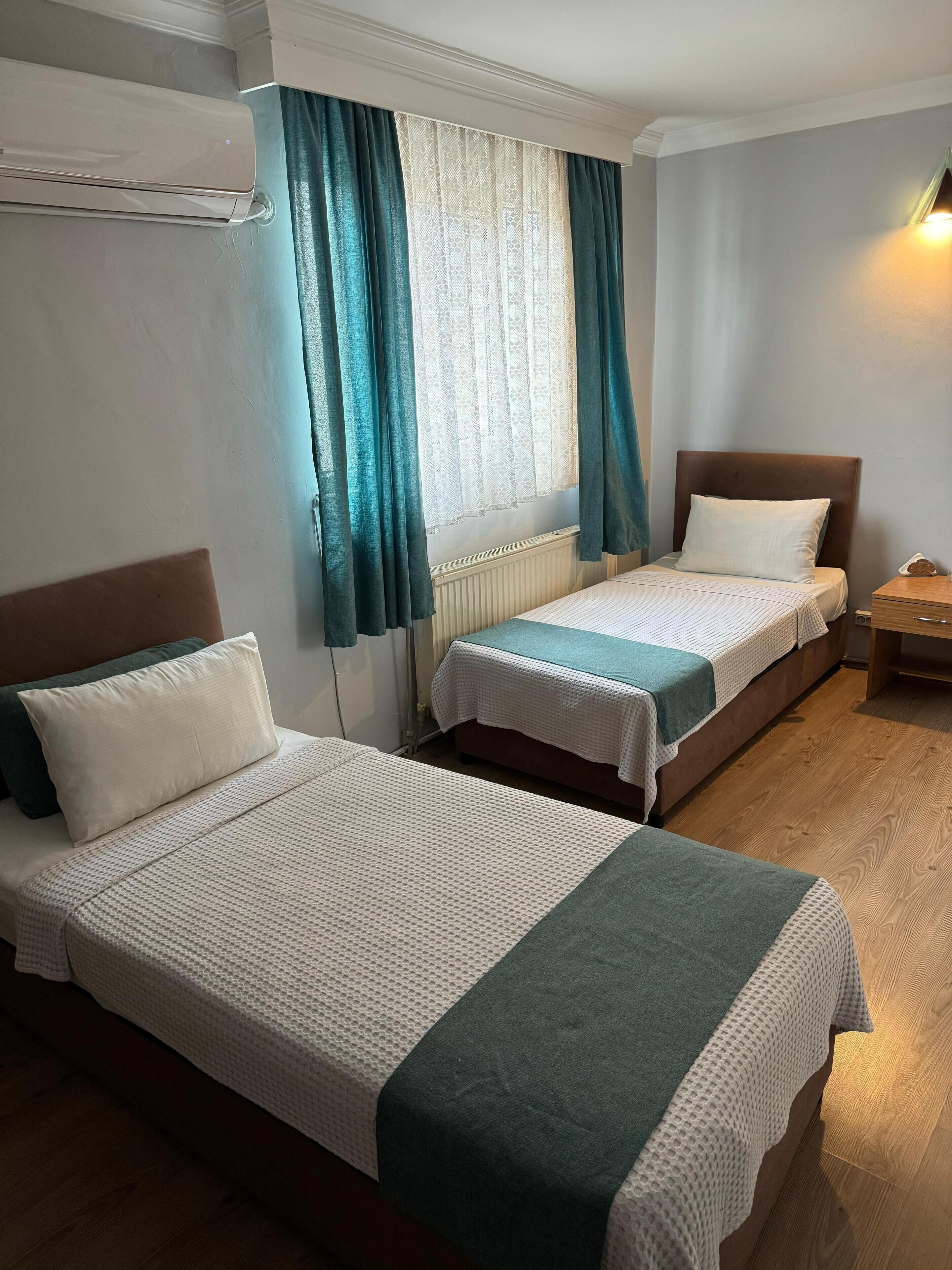 A room with two beds, a radiator, a window with curtains, and a wooden floor.