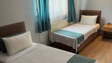 A room with two beds, a radiator, a window with curtains, and a wooden floor.