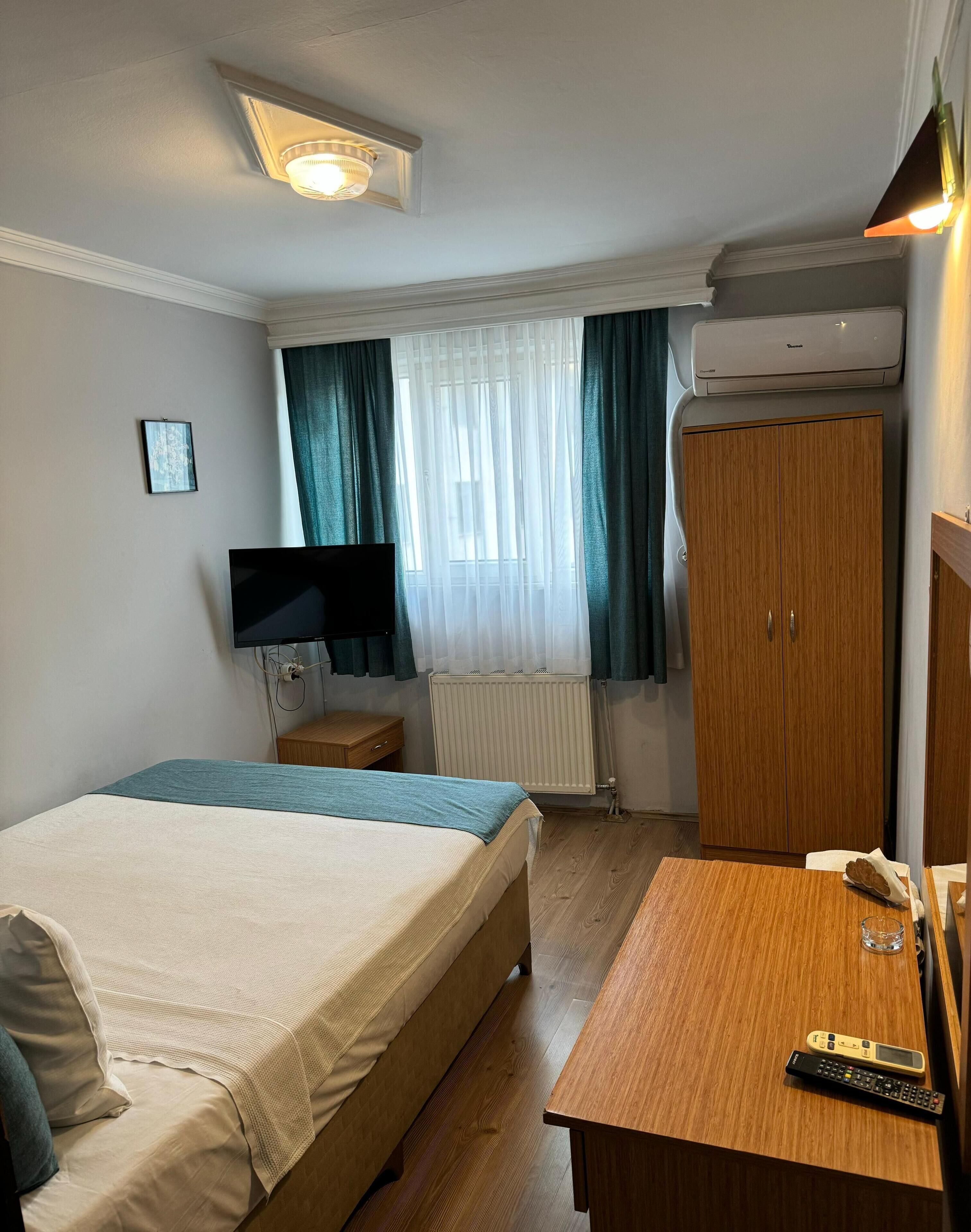 A hotel room with a bed, a desk, a TV, a wardrobe, and a radiator.