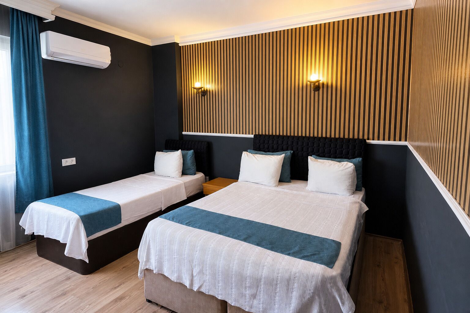 Habitación de hotel con dos camas individuales, una cama grande, aire acondicionado de pared y un panel de madera con una lámpara.