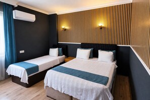 A hotel room with two single beds, a large bed, a wall-mounted air conditioner, and a wooden panel wall with a light fixture. - Elit Hotel Corlu (Corlu)