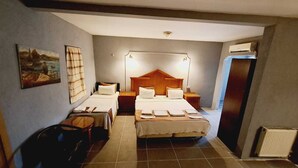 Une chambre d’hôtel avec deux lits simples, un lit double, une table de chevet avec une lampe, un tableau au mur et un radiateur.
