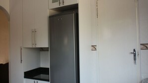 Een kleine keuken met witte kasten, een roestvrijstalen koelkast en een witte deur.
