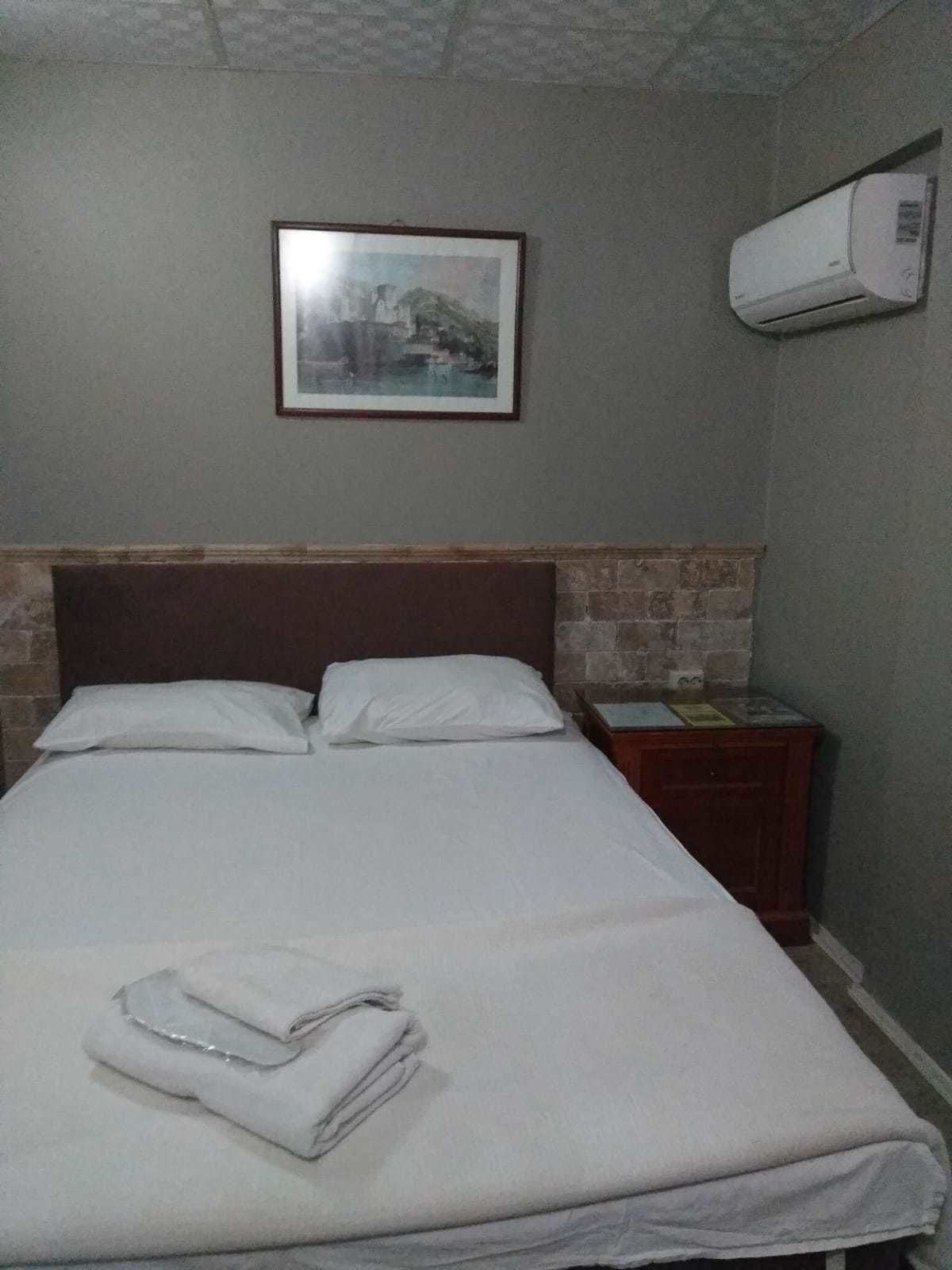 Una cama bien hecha con ropa blanca, un cuadro en la pared y un aire acondicionado de pared.