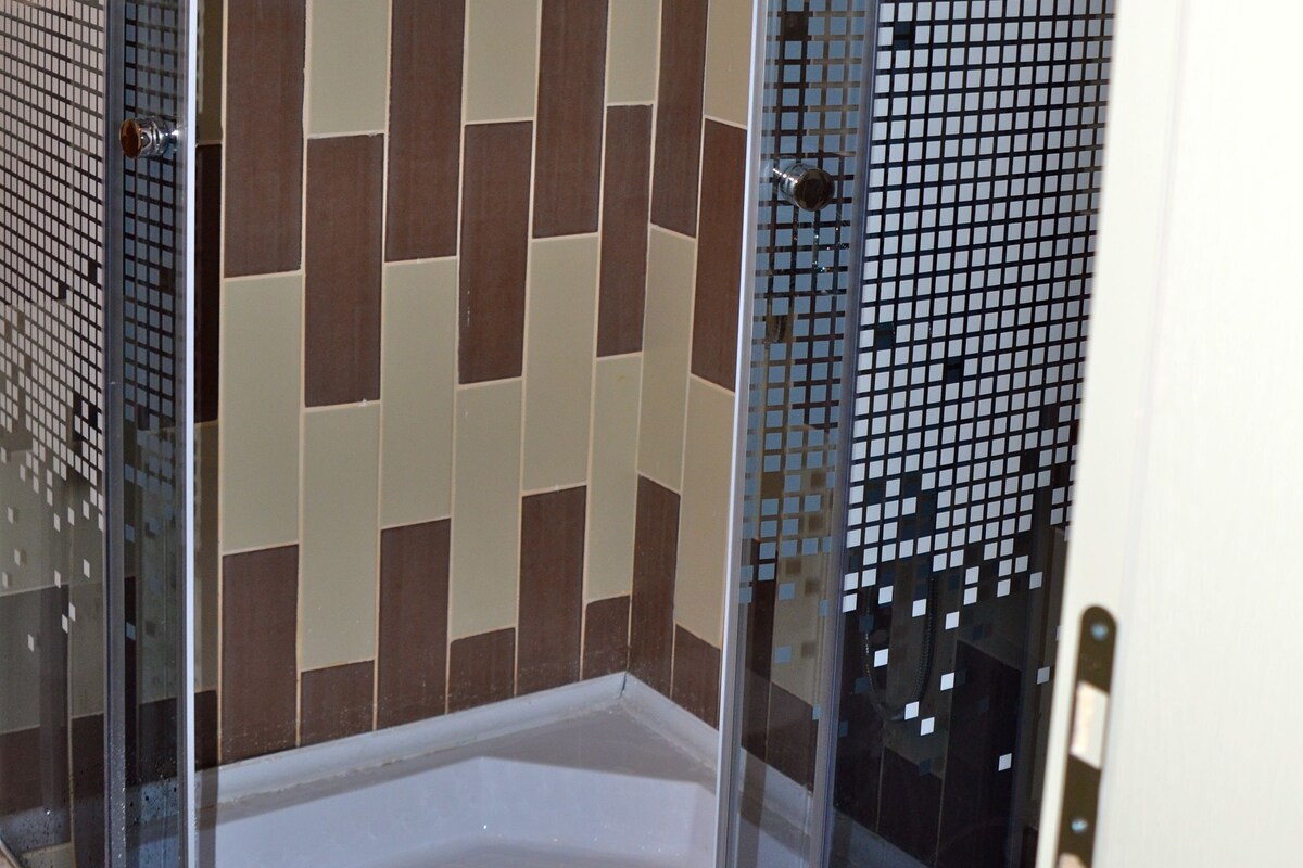 A glass-enclosed shower with a tiled wall featuring a geometric pattern.