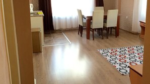 Un coin repas avec une table et des chaises, un coin cuisine avec une bouilloire, et un tapis à motifs sur le sol.
