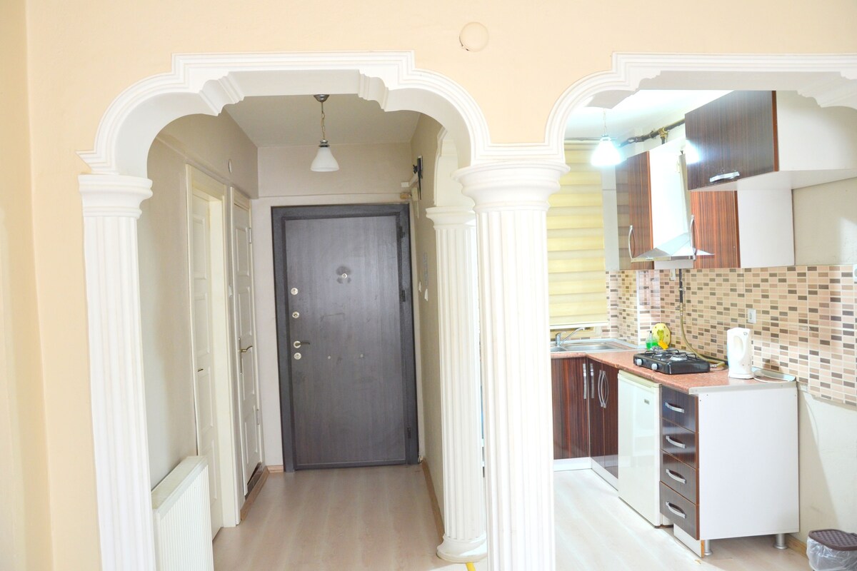 A hallway leading to a kitchen with white columns, a dark door, and a tiled backsplash.