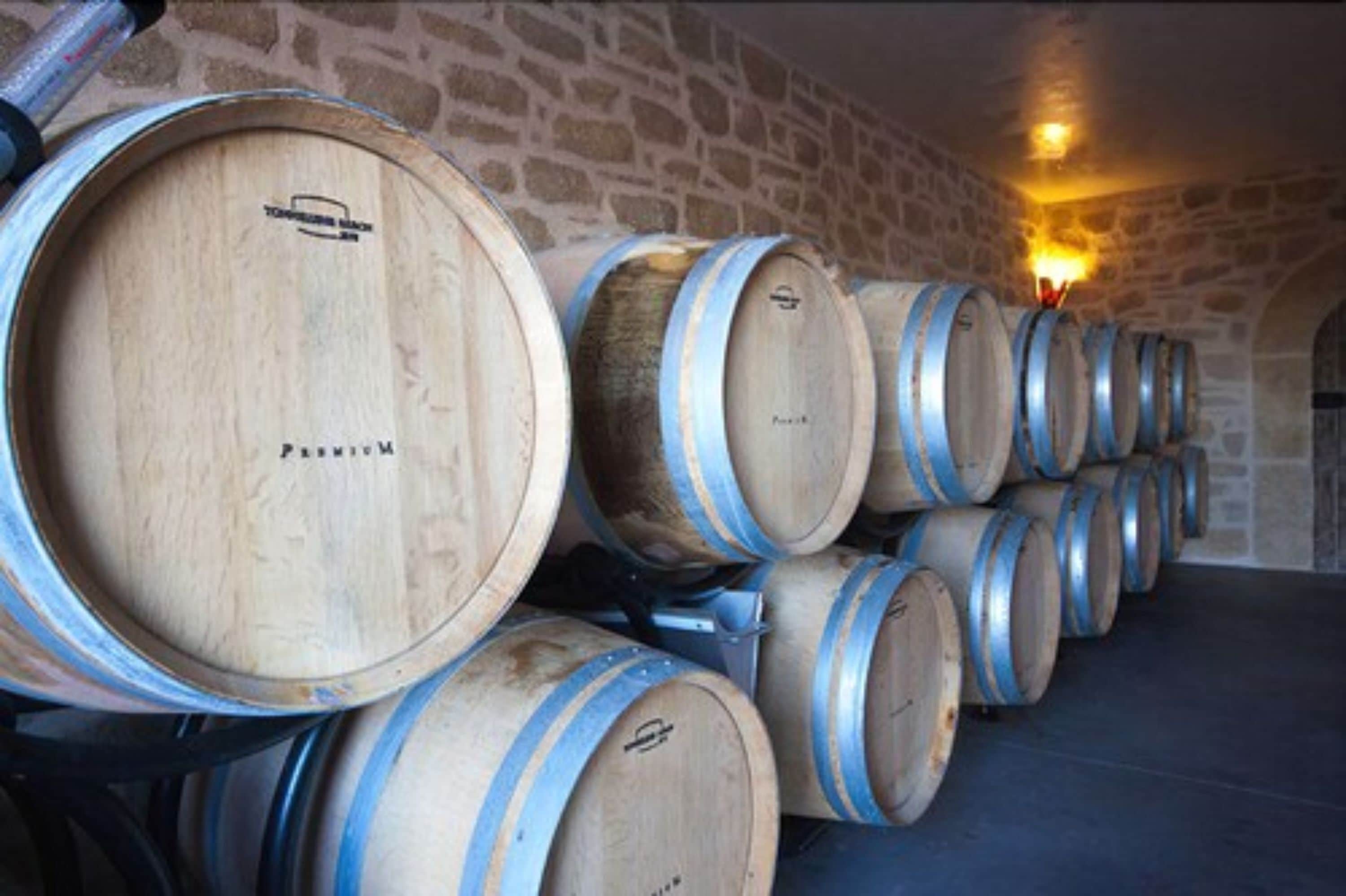 Wooden wine barrels stacked in a stone-walled cellar.