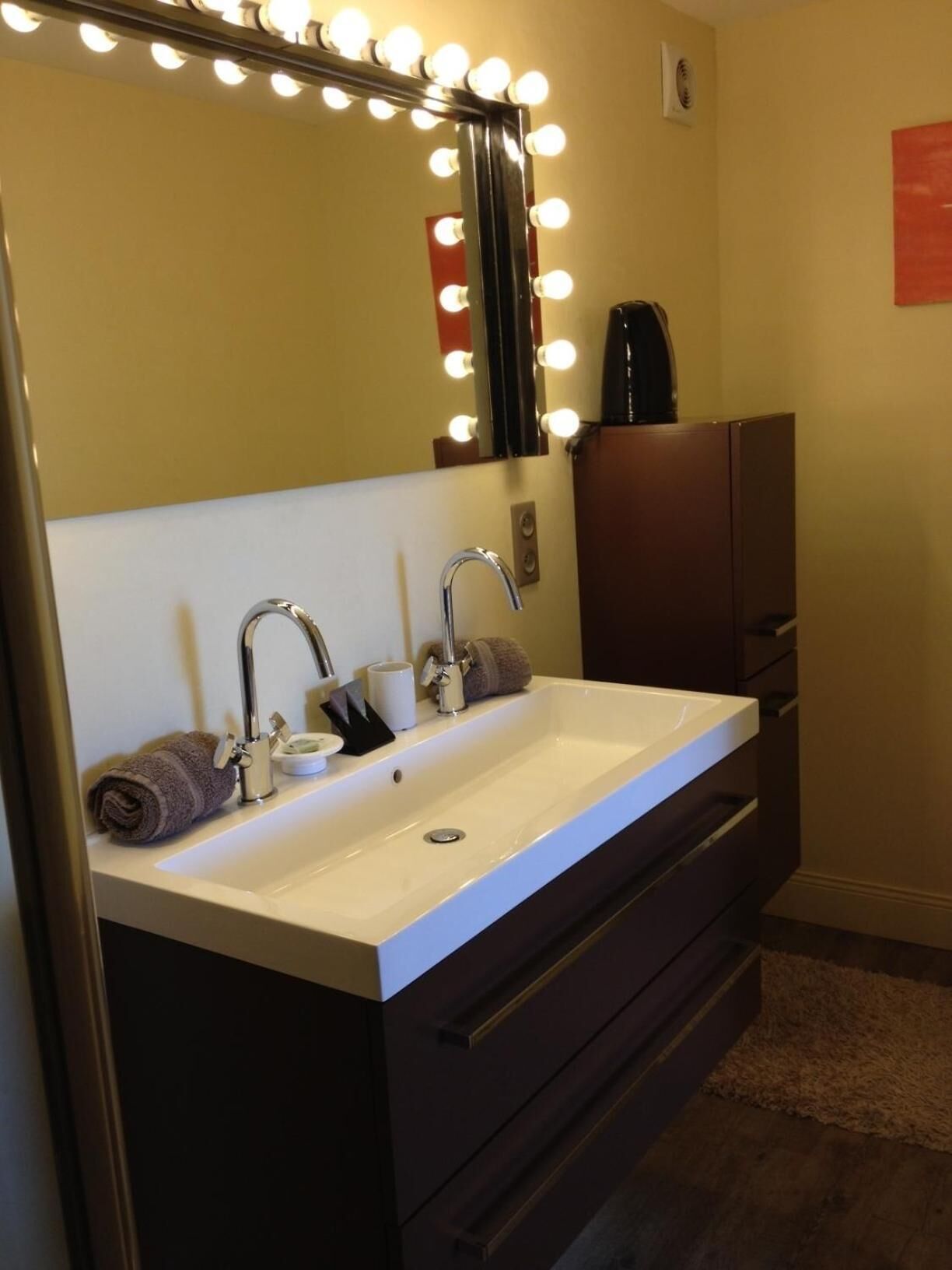 Une salle de bain comprenant un meuble-lavabo, un évier, un miroir avec éclairage et une serviette.