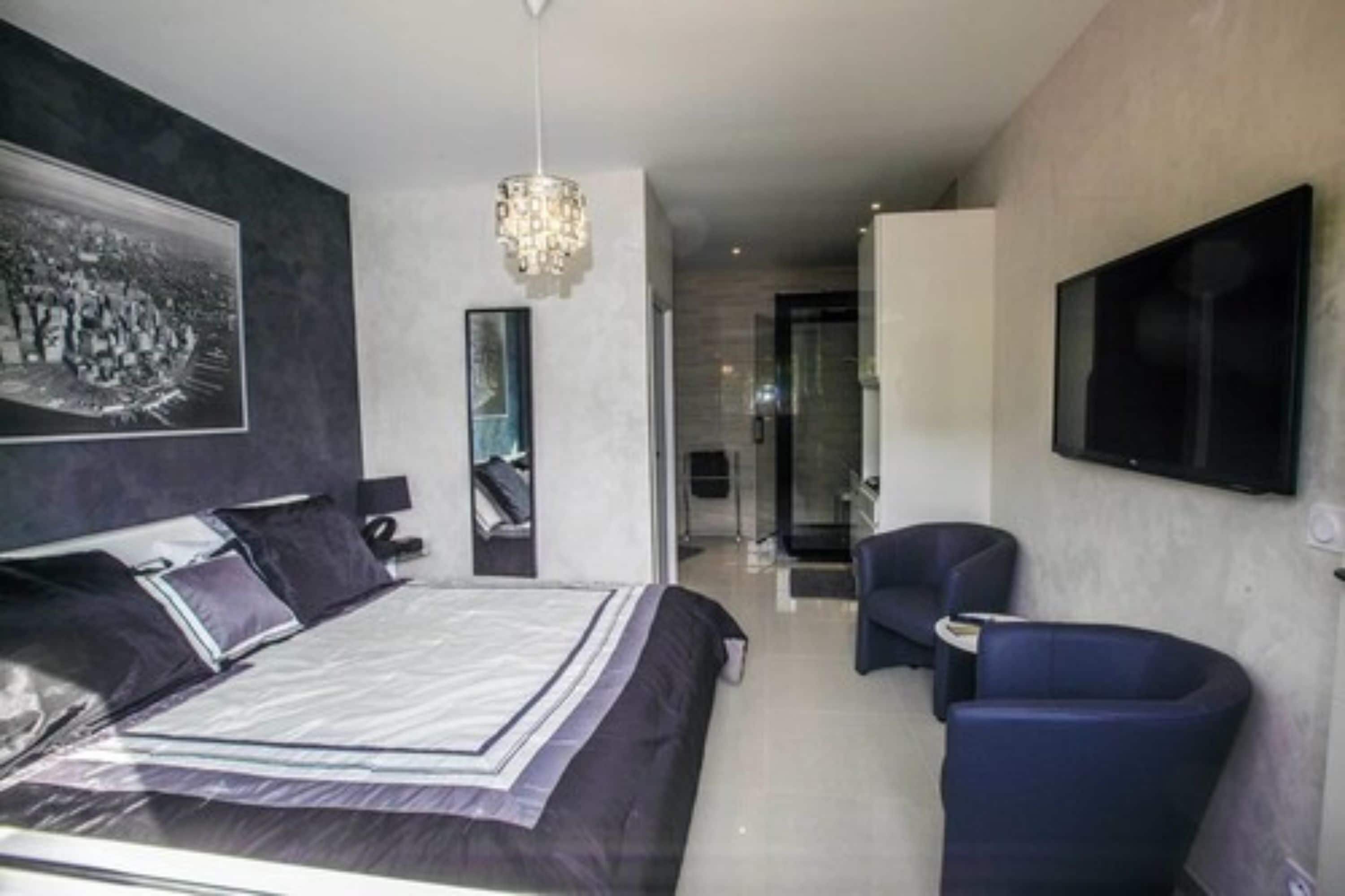 A modern hotel room with a large bed, a TV mounted on the wall, and a seating area with a chair.