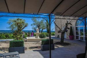 Un espacio al aire libre con patio y vista al mar, que incluye una pérgola, plantas en macetas y una zona de estar.