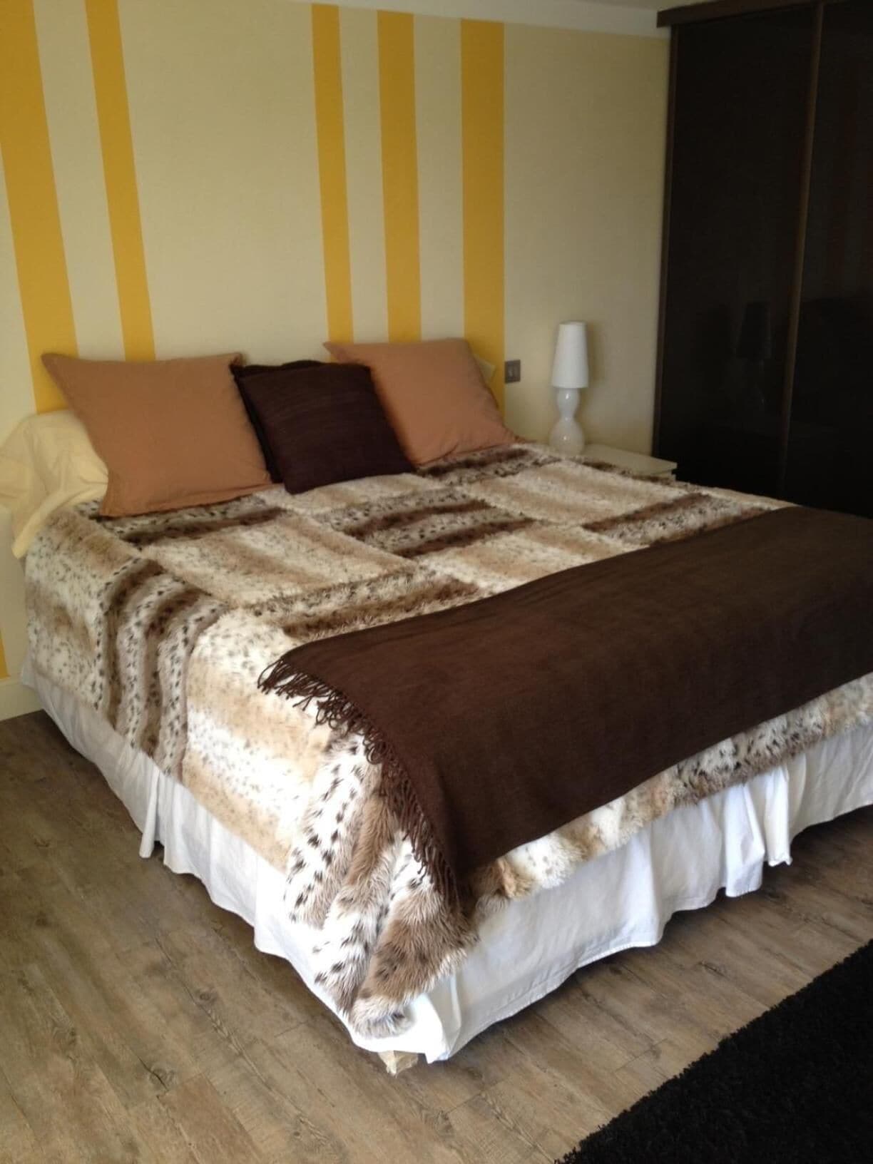 A bed with a patterned blanket and pillows, a bedside lamp, and a dark wardrobe.