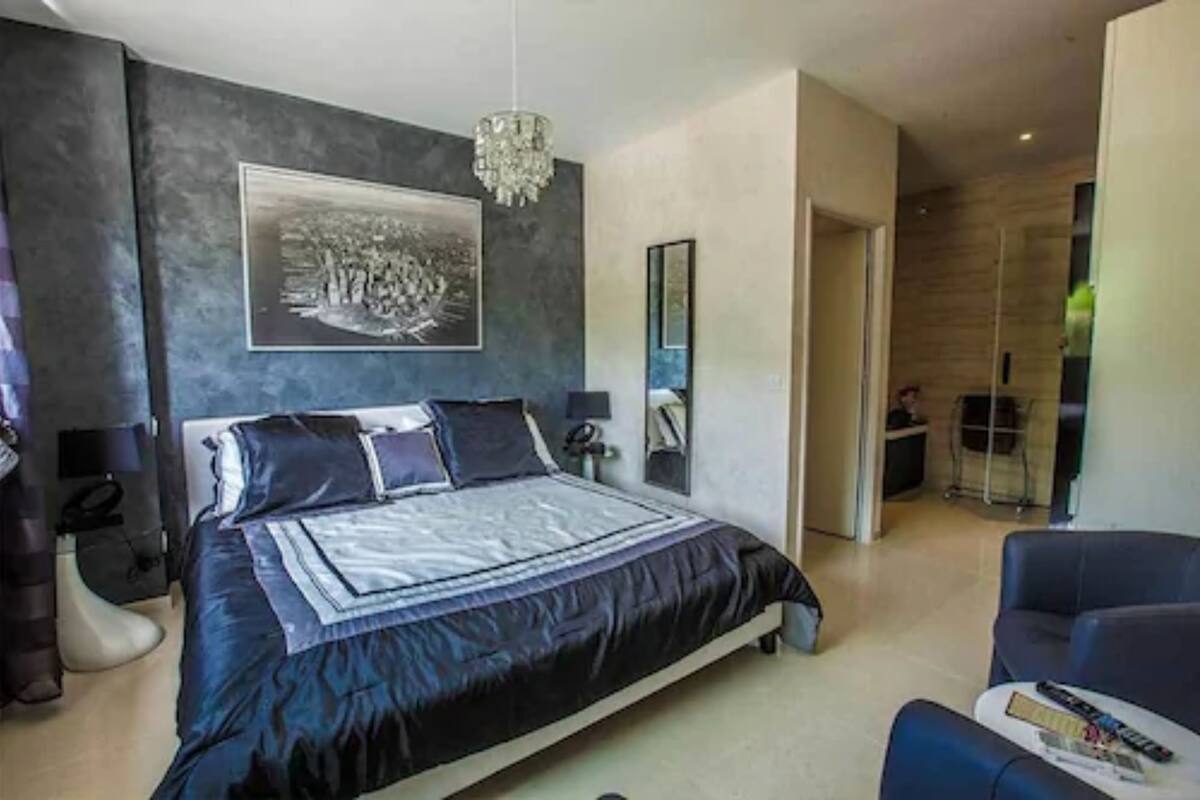 A modern bedroom with a large bed, a chandelier, a framed picture, and a mirror.