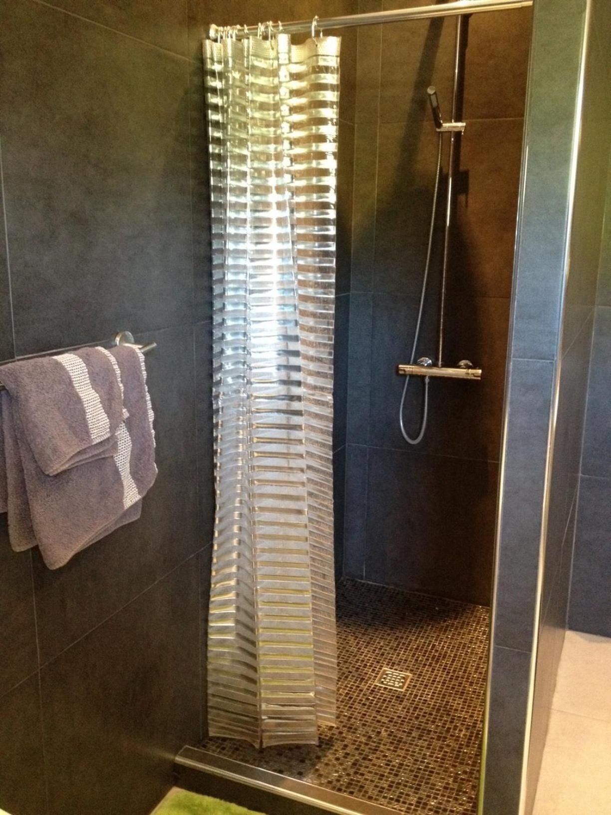 Zona de ducha con mampara de vidrio, toallero con toallas y ducha.
