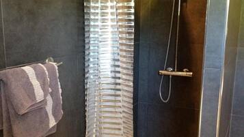 Zona de ducha con mampara de vidrio, toallero con toallas y ducha.