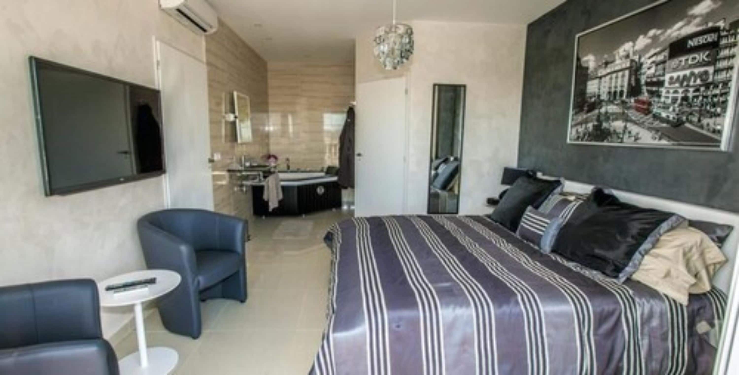 Ein modernes Hotelzimmer mit einem großen Bett, einer Sitzecke mit kleinem Tisch, einem separaten Badezimmer und einem an der Wand montierten Fernseher.