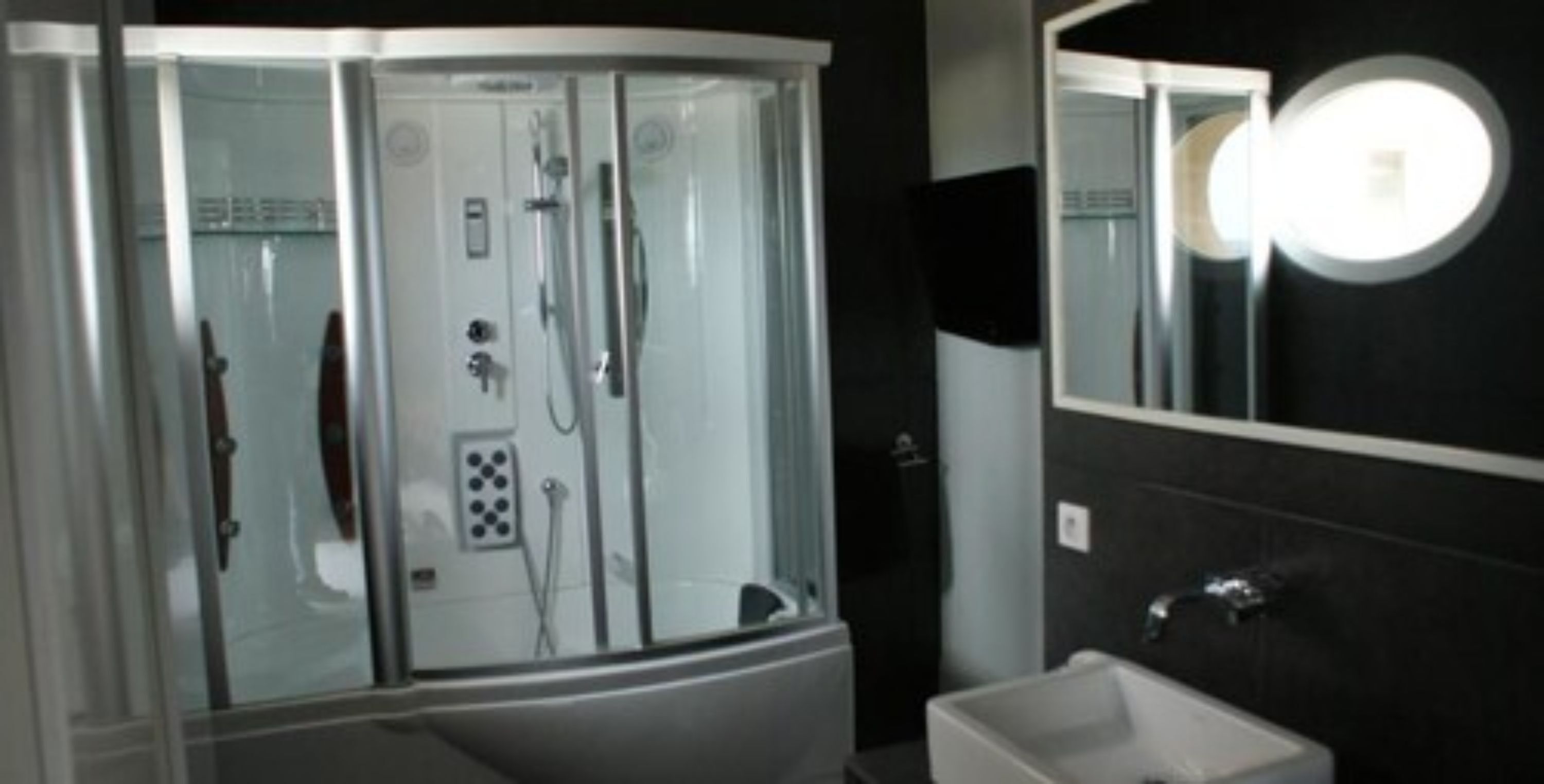 Une salle de bain moderne avec une douche à parois de verre, un lavabo blanc et un grand miroir.