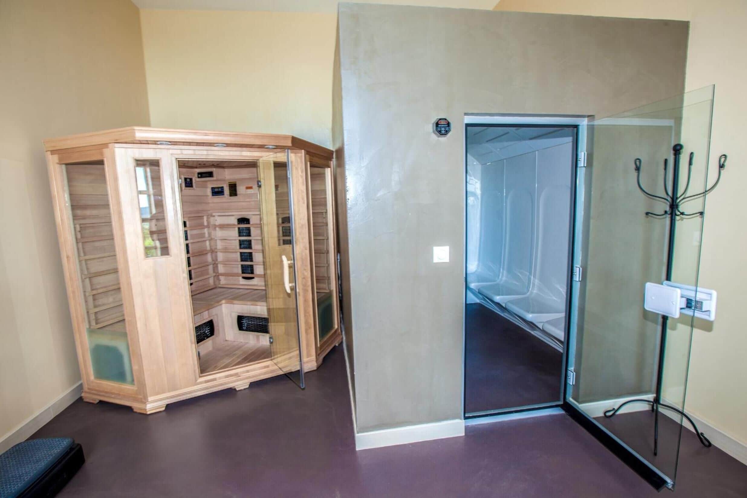 A room with a glass shower enclosure, a wooden sauna, and a glass door leading to a hallway.