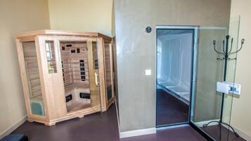 A room with a glass shower enclosure, a wooden sauna, and a glass door leading to a hallway.