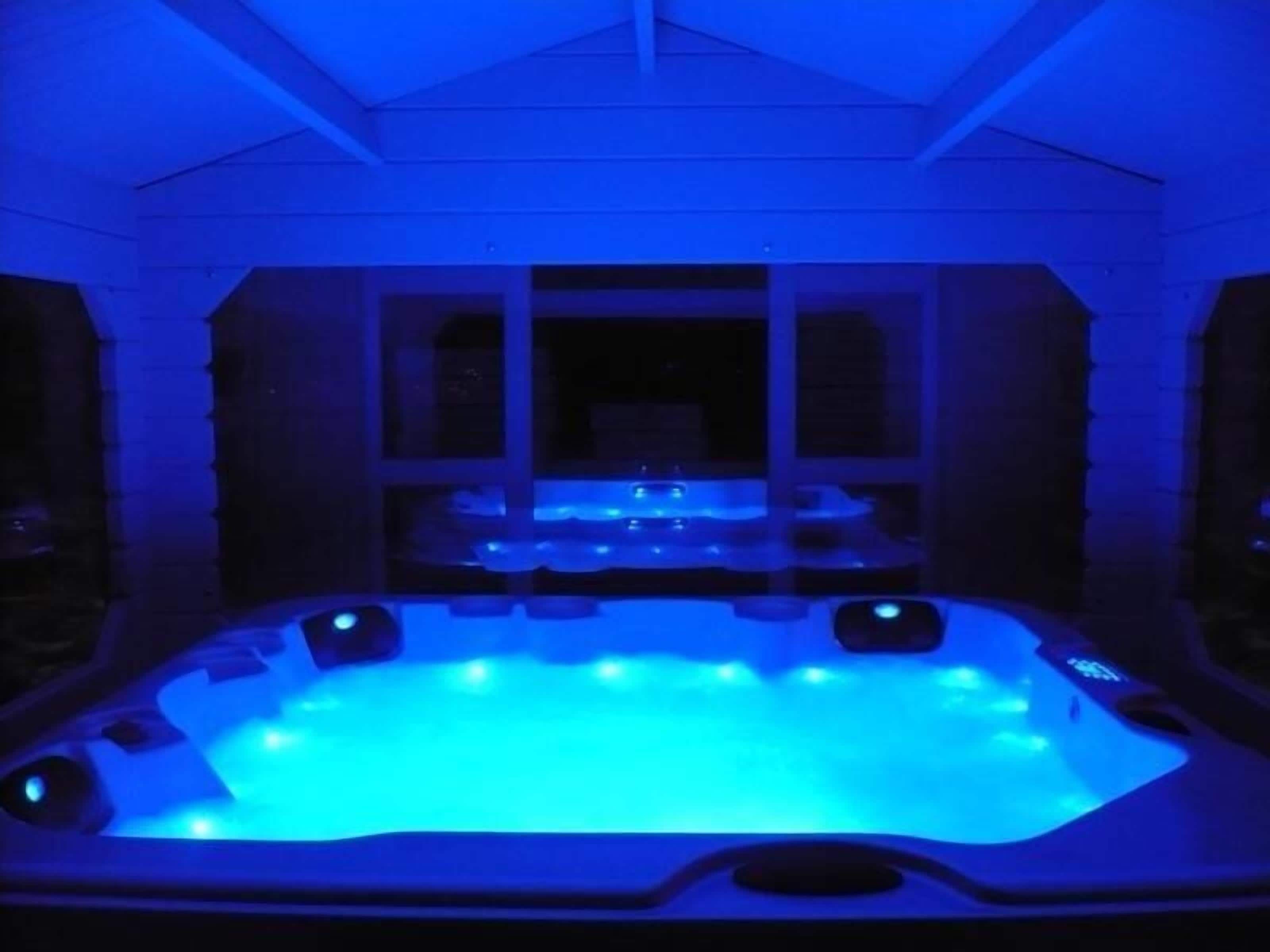 A hot tub with blue lighting, surrounded by a white exterior wall with windows.