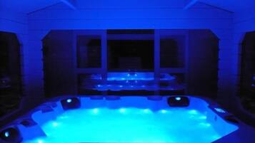 A hot tub with blue lighting, surrounded by a white exterior wall with windows.