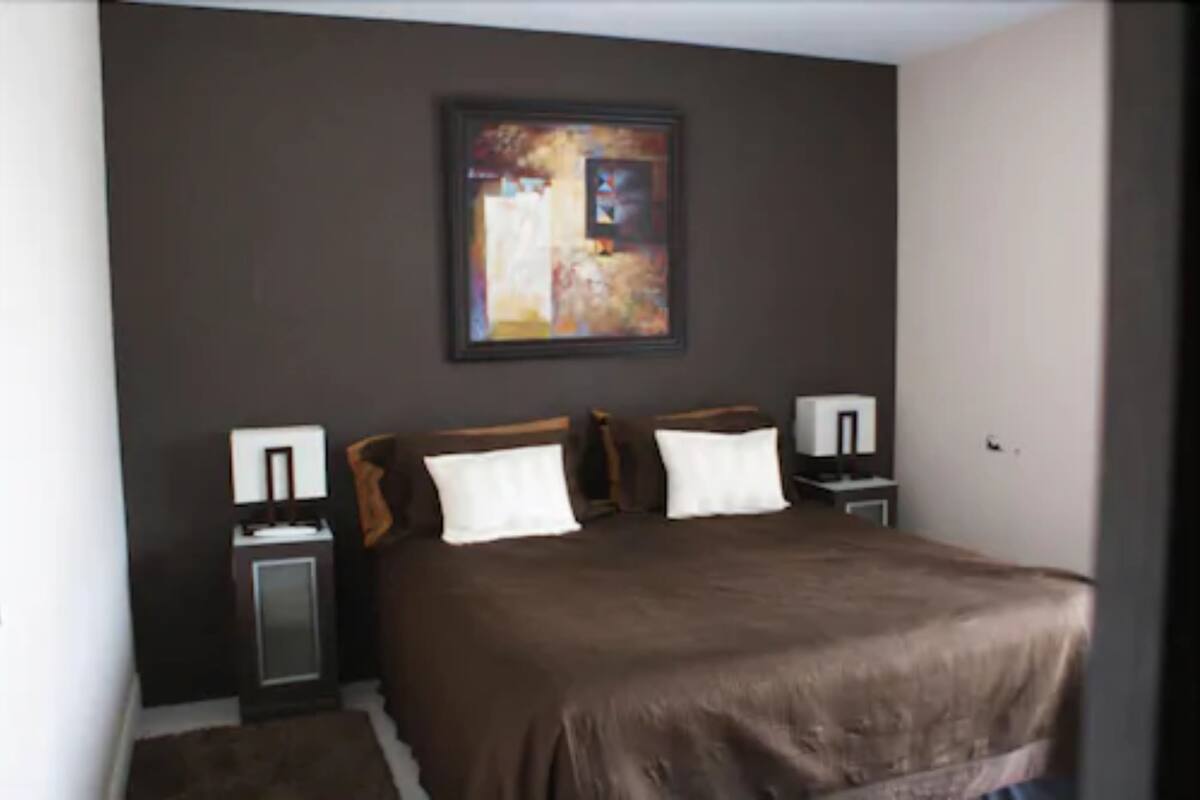 A bedroom with a large bed, two bedside tables, and a painting on the wall.