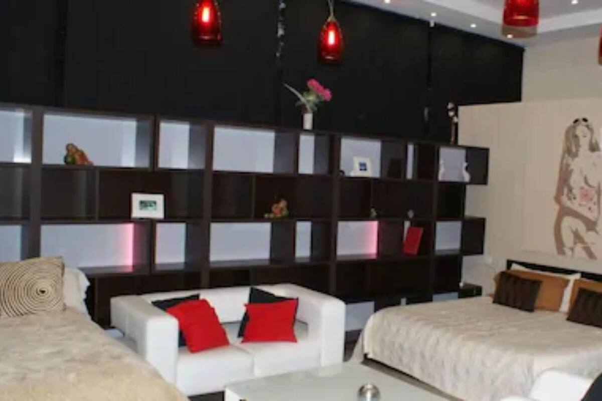 A modern hotel room with a large bed, a sofa, a desk, and a bookshelf.