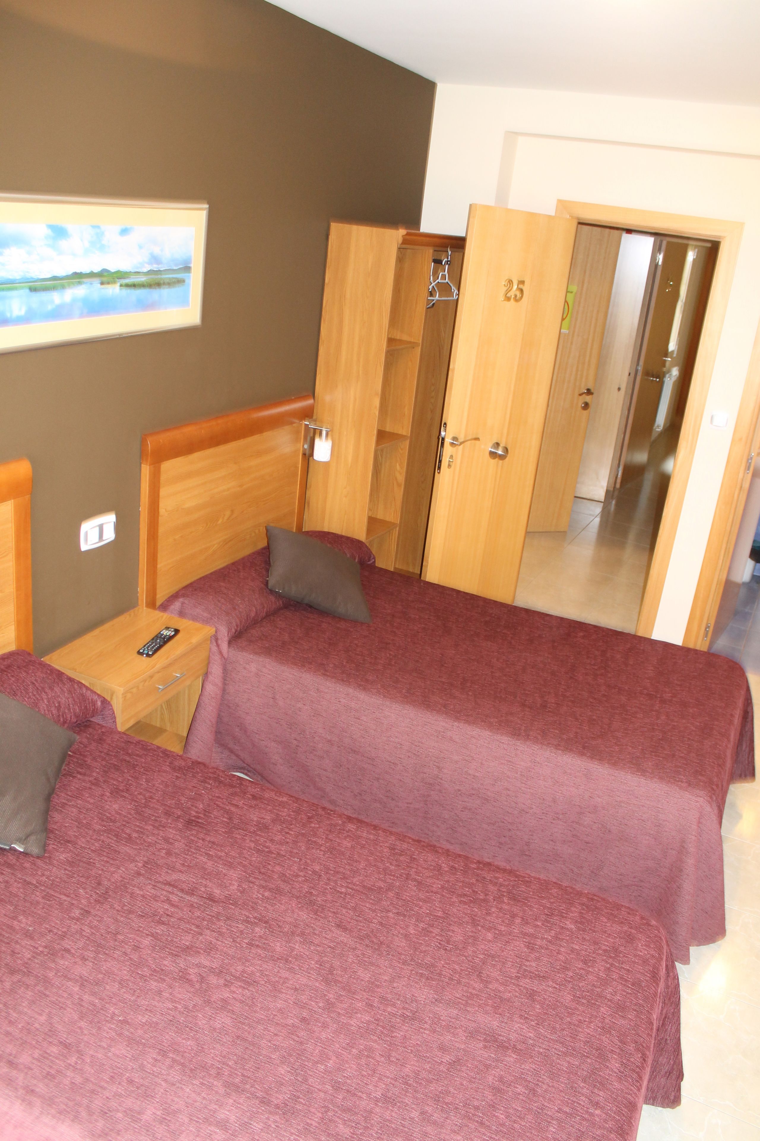 A hotel room with two beds, wooden wardrobes, a nightstand, and a painting on the wall.