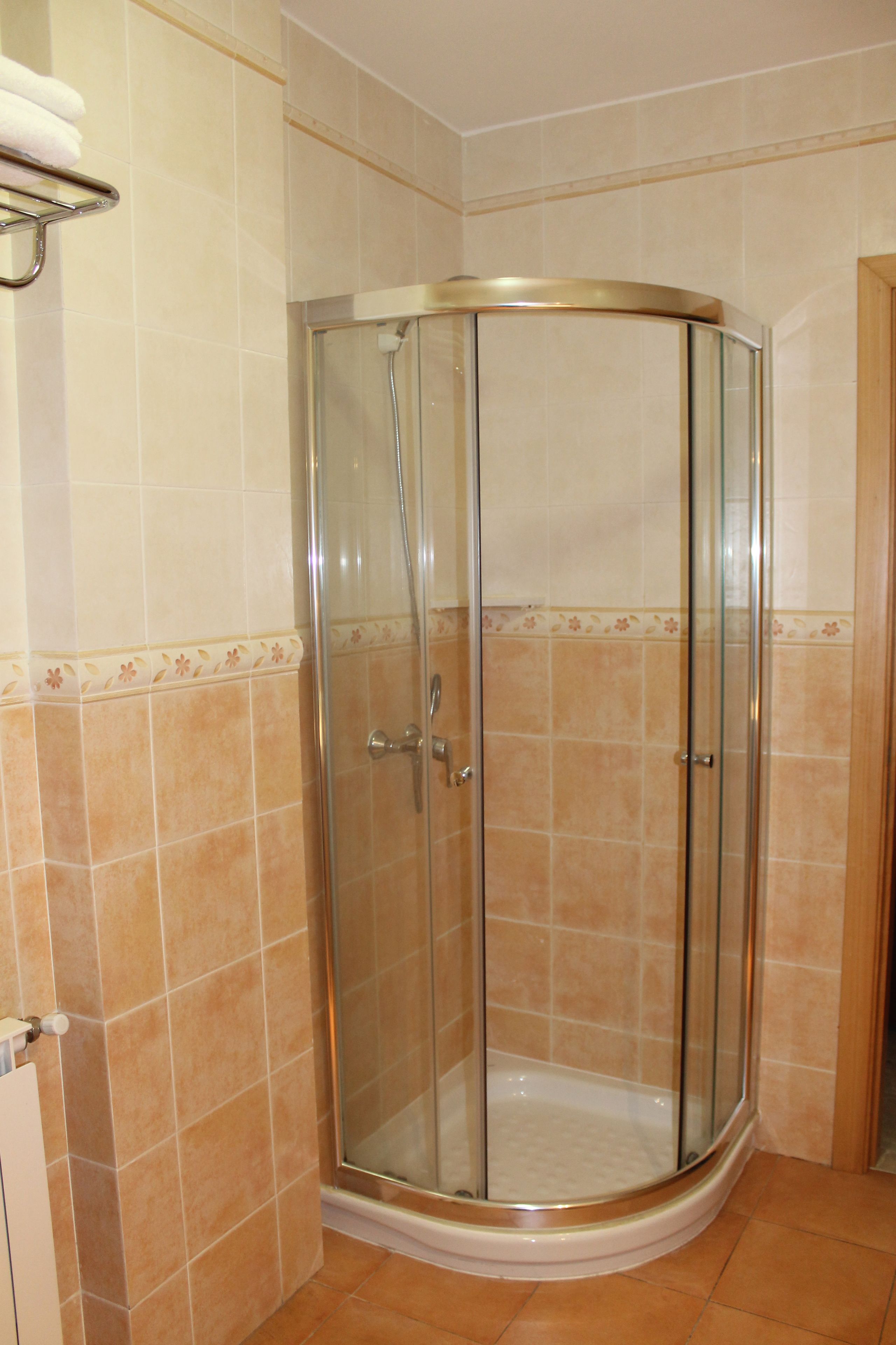 A glass-enclosed shower stall with a curved design, tiled walls, and a corner location.