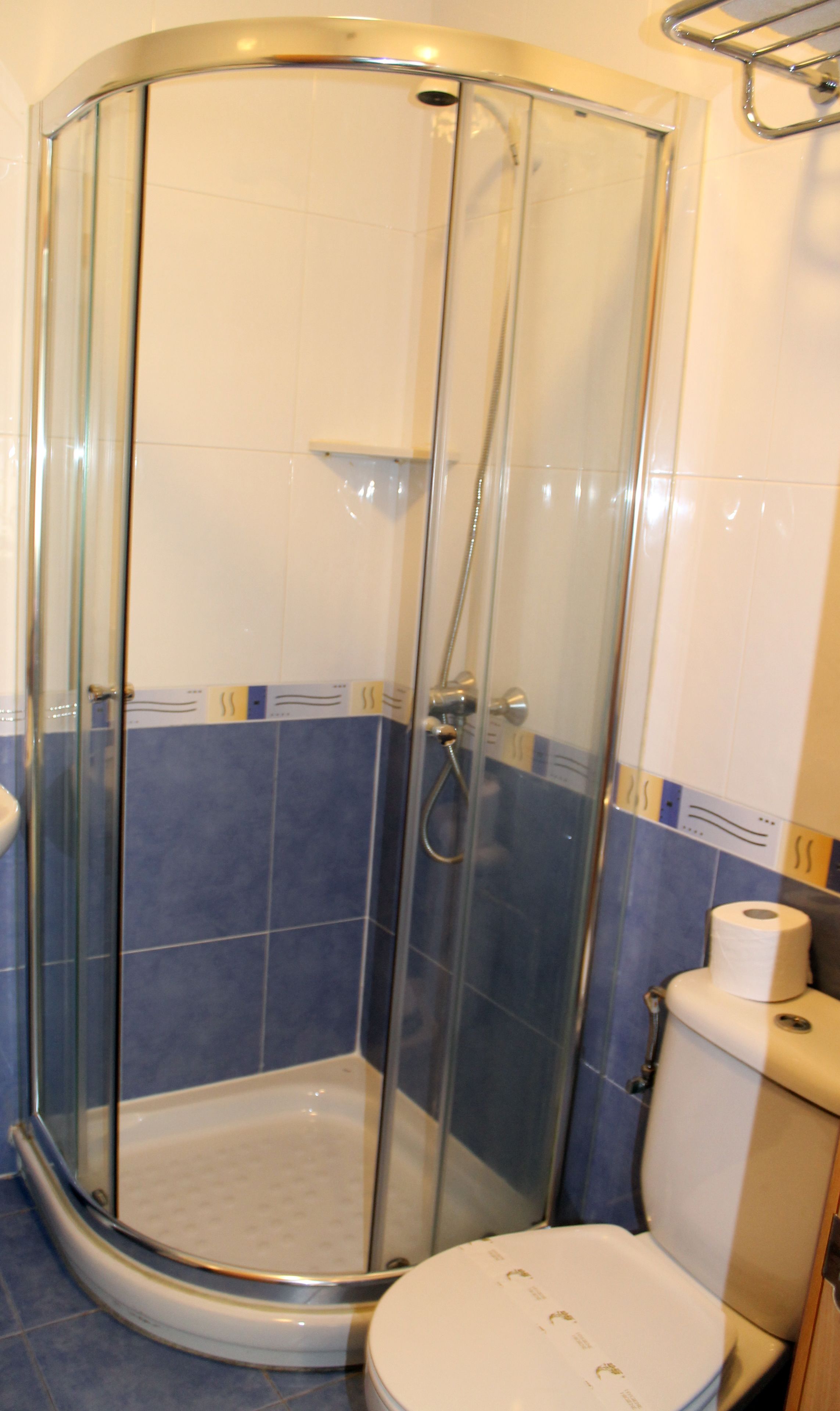 Box de chuveiro com paredes azulejadas em azul, vaso sanitário branco e divisória de vidro.