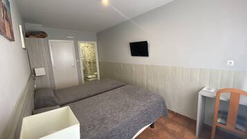 Una habitación con dos camas, un escritorio pequeño, una silla, un televisor y una puerta que da a un baño.