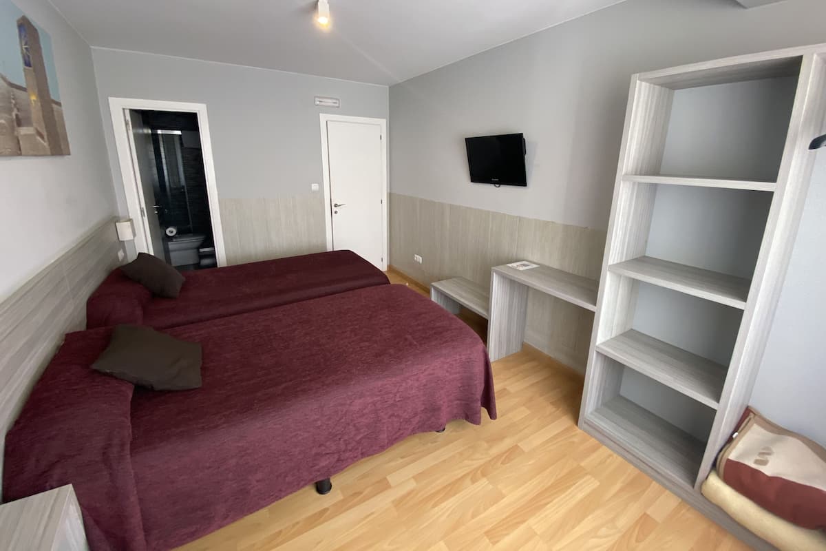 A bedroom with a bed, a TV mounted on the wall, and a wooden floor.