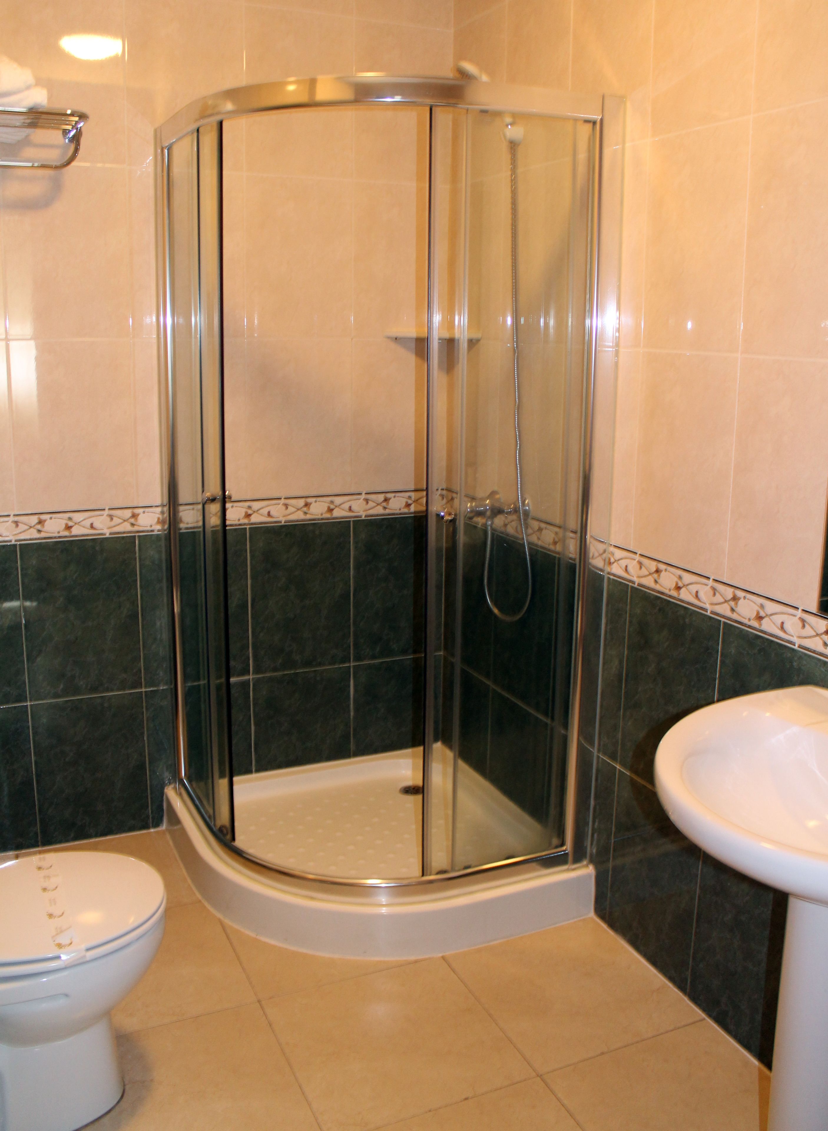 A glass-enclosed shower stall with a white sink and toilet in a bathroom with beige and dark tiles.