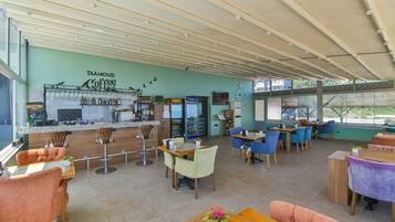 A spacious coffee shop with a bar area, multiple seating options including bar stools and tables, and a large window offering a view of the outdoors.