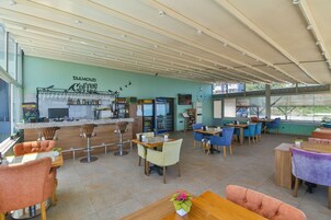 Una amplia cafetería con zona de bar, diversas opciones de asientos que incluyen taburetes y mesas, y un gran ventanal con vistas al exterior.