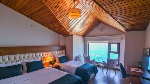 A hotel room with two beds, a desk, a chair, a lamp, and a view of the sea. - Diamond Hotel (Amasra)