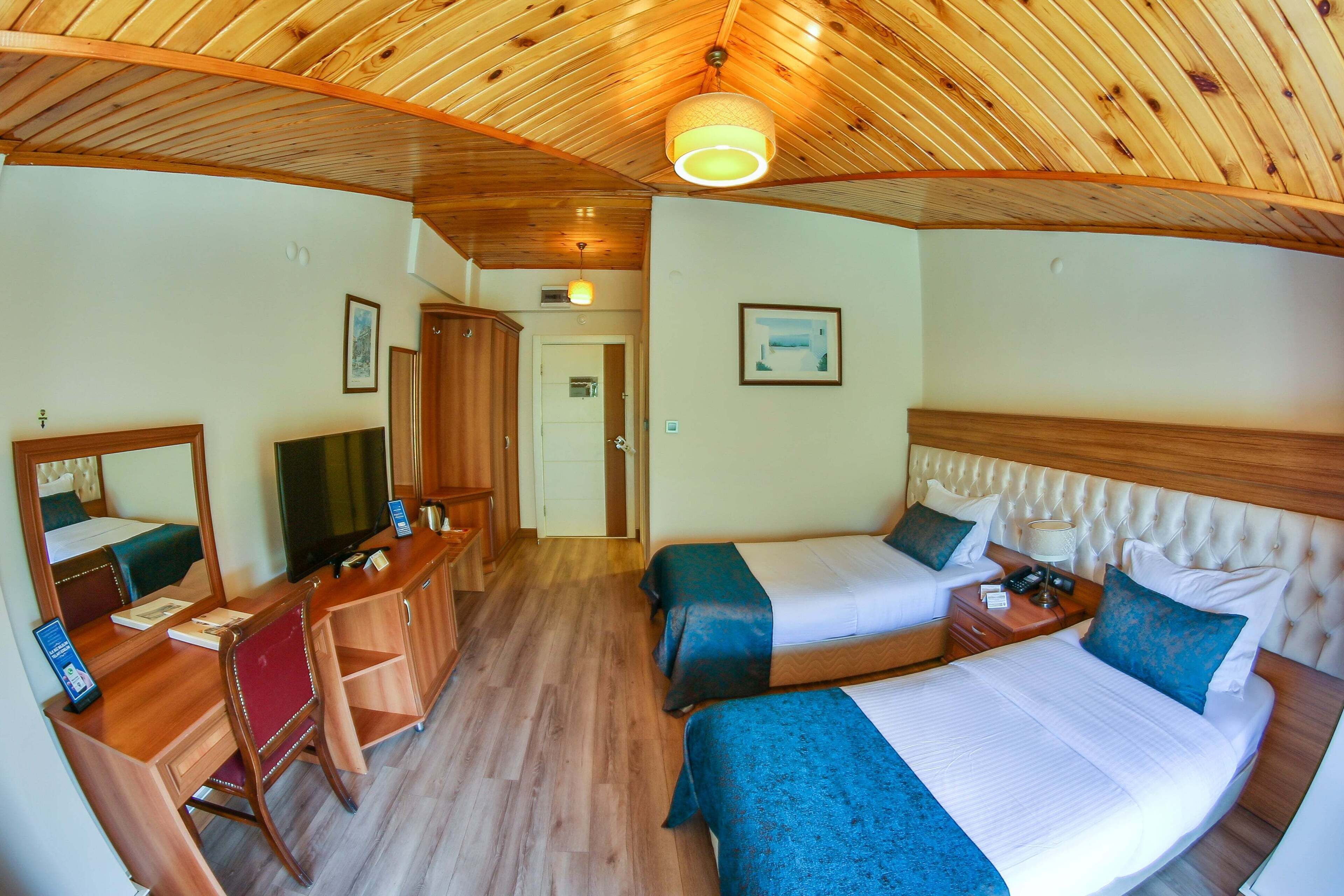 A hotel room with two beds, a desk with a chair, a television, and a wooden ceiling.