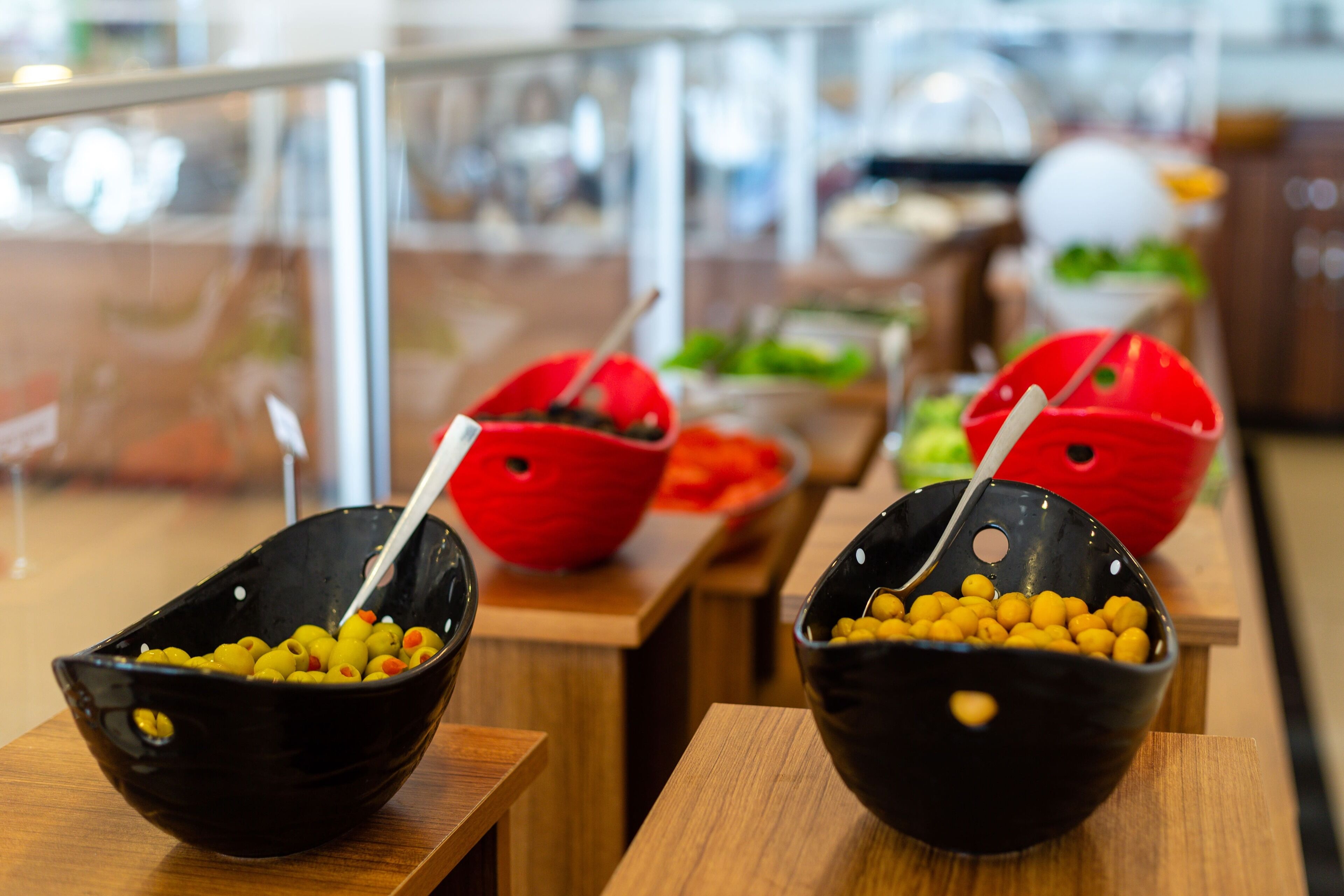Un buffet avec des bols noirs contenant des olives et des pois chiches, et des bols rouges avec des légumes.