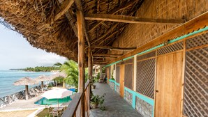 A wooden balcony with a thatched roof overlooking a pool and beach. - Yoset Hotel (Cayes-Jacmel)