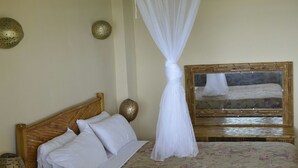 A bedroom with a wooden headboard, a bed with white bedding, a floral-patterned bedspread, and a white canopy. - Yoset Hotel (Cayes-Jacmel)