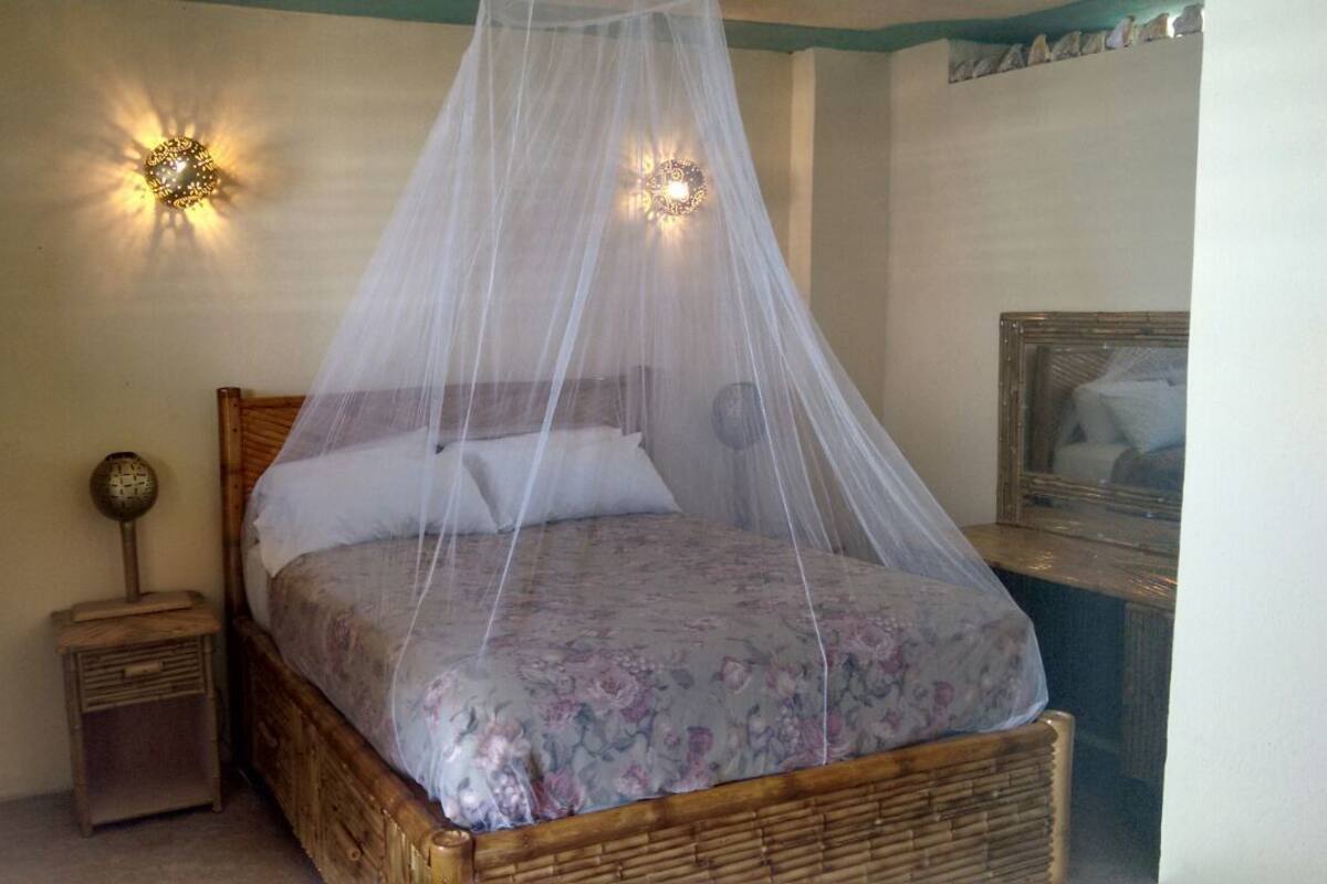 A bed with a floral bedspread and a canopy, a small bedside table, and wall-mounted lights.