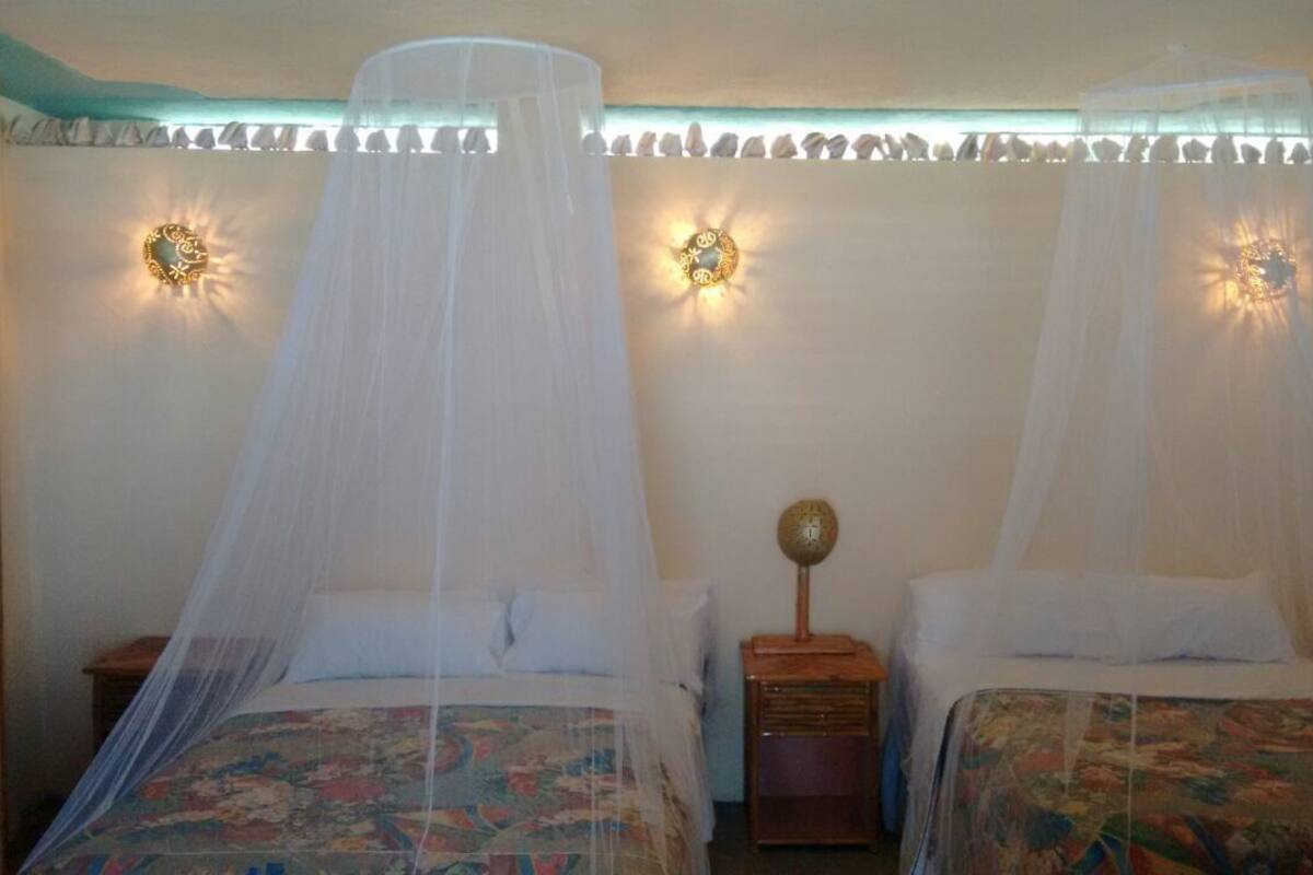 A room with two beds, each with a canopy. There are wall sconces and a small table between the beds.