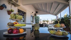 Une présentation de fruits variés, disposés sur des présentoirs à plusieurs niveaux, avec un ananas comme pièce maîtresse, et une vue sur l’extérieur.