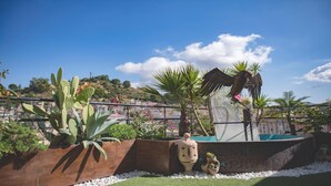Un jardín con un cactus, palmeras y una escultura de un pájaro.